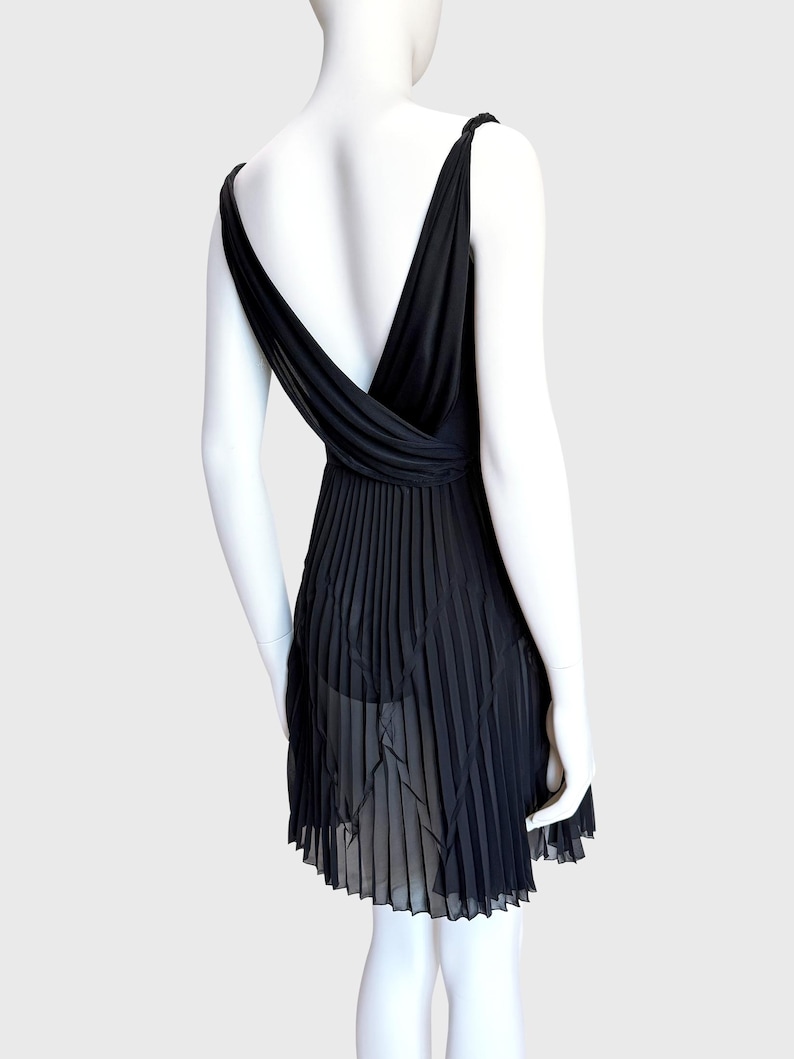 K&ouml;nnte beinhalten: Schwarzes Kleid mit tiefem V-Ausschnitt und plissiertem Rock. Das Kleid hat einen tiefen R&uuml;cken und d&uuml;nne Tr&auml;ger. Der Rock hat ein transparentes, geschichtetes Design. Das Kleid wird auf einer Schaufensterpuppe pr&auml;sentiert.