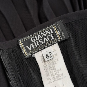 K&ouml;nnte beinhalten: Nahaufnahme eines schwarzen Kleidungsst&uuml;cks mit einem Etikett "GIANNI VERSACE COUTURE". Das Etikett zeigt Gr&ouml;&szlig;e 42 und Stoffzusammensetzung. Das Kleidungsst&uuml;ck hat eine plissierte Textur.