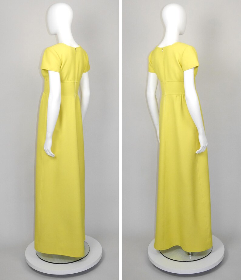 May include: A bright yellow, floor-length dress with short sleeves and a fitted waist. The dress is displayed on a mannequin, showcasing its simple, elegant design. The dress has a round neckline and a subtle A-line skirt.