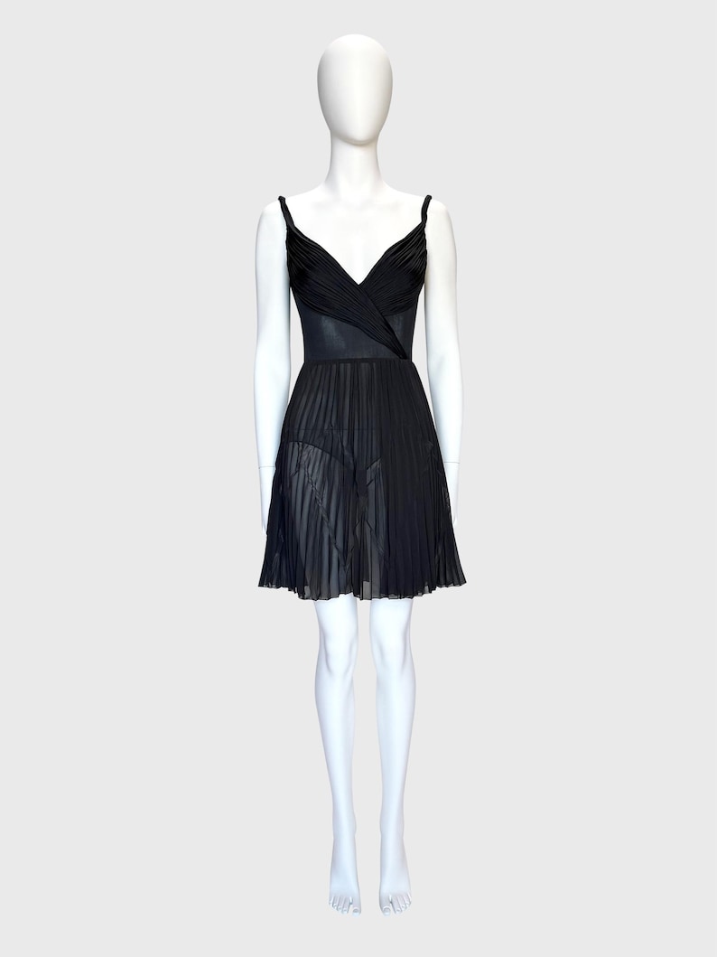 K&ouml;nnte beinhalten: Ein schwarzes Kleid auf einer Schaufensterpuppe. Das Kleid hat ein V-Ausschnitt-Oberteil mit Spaghettitr&auml;gern und einen plissierten Rock. Das Oberteil scheint aus einem strukturierten Stoff zu sein, w&auml;hrend der Rock ein durchsichtiges, flie&szlig;endes Material ist.