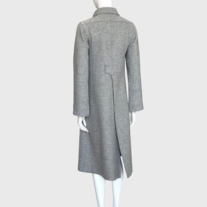 May include: A gray, long coat with a notched collar and a split back hem. The coat has long sleeves and a tailored fit, displayed on a mannequin. The coat is made of a textured fabric.