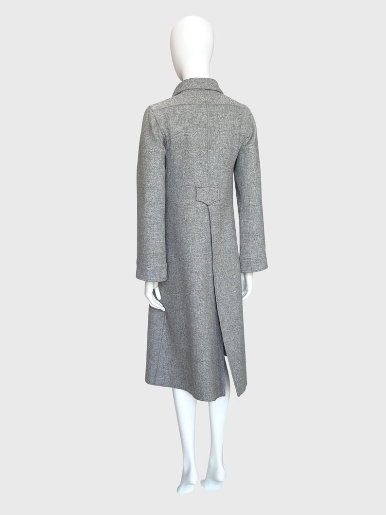 May include: A gray, long coat with a notched collar and a split back hem. The coat has long sleeves and a tailored fit, displayed on a mannequin. The coat is made of a textured fabric.