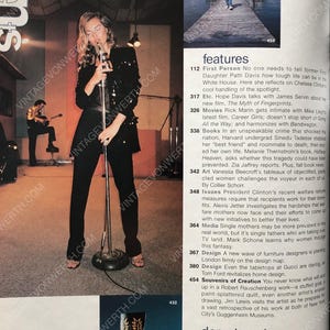 May include: A black and white photo of a woman singing into a microphone in a recording studio. The woman is wearing a black sequined top and black pants. The microphone is on a stand. The background is a white wall with a window. The photo is from a magazine article about the woman's career.