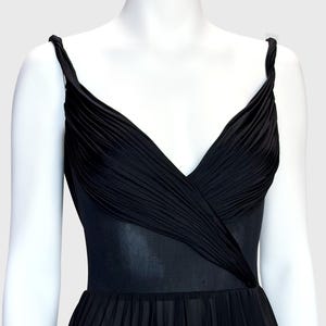 K&ouml;nnte beinhalten: Schwarzes Kleid mit V-Ausschnitt und plissiertem Rock. Das Oberteil hat ein drapiertes Design und das Kleid hat d&uuml;nne Tr&auml;ger. Das Kleid wird auf einer wei&szlig;en Schaufenquin vor hellem Hintergrund pr&auml;sentiert.