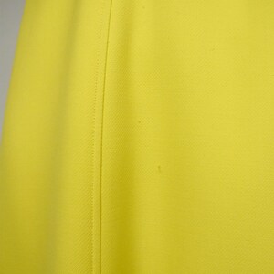 May include: Close-up of a bright yellow fabric with a subtle textured pattern. A vertical seam runs down the center, creating a tailored look. The fabric appears to be a solid color, with no visible patterns or designs.