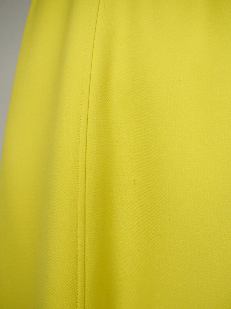 May include: Close-up of a bright yellow fabric with a subtle textured pattern. A vertical seam runs down the center, creating a tailored look. The fabric appears to be a solid color, with no visible patterns or designs.