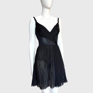 K&ouml;nnte beinhalten: Ein schwarzes Kleid mit V-Ausschnitt und Spaghettitr&auml;gern. Das Oberteil hat ein drapiertes Design und der Rock ist plissiert. Das Kleid wird auf einer wei&szlig;en Schaufensterpuppe vor wei&szlig;em Hintergrund pr&auml;sentiert.