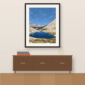 Guitar Lake gouache-style vertical print in a dark frame above a wooden sideboard, shown as a room mockup