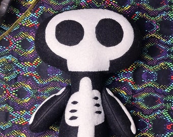 May include: A black and white plush toy shaped like a skeleton with a skull head. The toy has a white skeleton design on a black background.