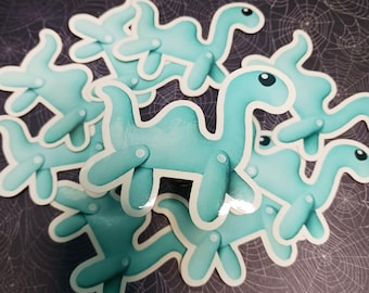 Può includere: Una collezione di adesivi a forma di cammello azzurro con effetto acquerello. Ogni adesivo presenta un disegno di cammello con arti articolati e un bordo bianco. Gli adesivi sono sparsi su uno sfondo scuro con un motivo a ragnatela.