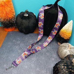 May include: Purple lanyard with a repeating pattern of a cartoon character with yellow eyes and a red nose. The lanyard has a metal clasp.