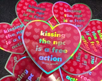Può includere: Una collezione di adesivi a forma di cuore con sfondo rosso e piccoli motivi a cuore. Gli adesivi presentano il testo "Kissing the npc is a free action" in un carattere olografico color arcobaleno. È visibile anche il testo "Crypto Arcade".