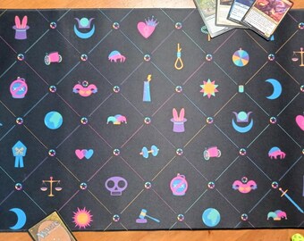 Può includere: Un tappetino da gioco rettangolare nero con un motivo a rombi ripetuto e icone colorate tra cui cuori, lune, stelle, bilance, teschi e cilindri con orecchie di coniglio in tonalità rosa, blu e giallo.