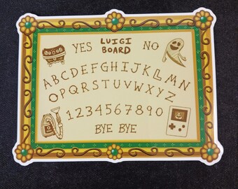 Può includere: Un adesivo rettangolare con un design Luigi Board, un centro color marrone chiaro e un bordo floreale decorativo dorato e verde. La tavola include l'alfabeto, i numeri 0-9, le parole YES, NO, BYE BYE, oltre a illustrazioni di un forziere, un fantasma, un aspirapolvere e una console portatile.