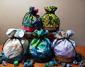 Può includere: Cinque sacchetti in tessuto con chiusura a coulisse, caratterizzati da vari motivi colorati e basi a tinta unita. Le borse presentano cordini neri e sono circondate da dadi da gioco poliedrici sparsi su una superficie in legno.