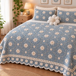 May include: A light blue crochet bedspread and two matching pillow shams featuring a repeating pattern of cream-colored daisy motifs. The set includes a decorative, three-dimensional flower-shaped pillow in cream with a textured center.