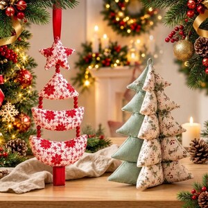 May include: A hanging ornament featuring a red and white poinsettia fabric star and crescent shapes connected by red beads, alongside a standing fabric Christmas tree ornament with alternating sage green and floral patterned triangular tiers.