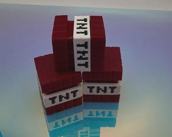 May include: A stack of three red block-shaped items resembling dynamite sticks. Each block features a white band around the centre with the black text TNT printed on it. The objects have a textured surface and are arranged in a pyramid formation.