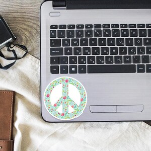 A peace sign sticker with a floral pattern in shades of pink, green, and blue on a silver laptop.
