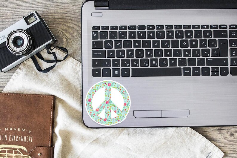 A peace sign sticker with a floral pattern in shades of pink, green, and blue on a silver laptop.