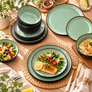 May include: A set of mint green ceramic dinnerware featuring a speckled finish and dark brown rims. The collection includes multiple plates and bowls, some stacked and others containing prepared food like salmon, salad, and shrimp pasta.