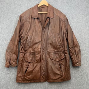 May include: A brown leather jacket featuring a collared neckline, a full-length front zipper closure, long sleeves with buttoned cuffs, two chest pockets, and two lower flap pockets with a cinched waist design.
