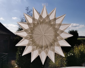 Könnte beinhalten: Ein transparenter weißer Papierstern als Dekoration mit mehreren scharfen, spitzen Strahlen, die in einem symmetrischen, geschichteten geometrischen Muster angeordnet sind und eine komplexe Faltstruktur aufweisen.