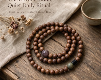 May include: A long strand of hand-polished natural wood beads arranged in a circular coil. The necklace features a single purple striped bead, a green bead, and three small black beads. Text reads: Warm Wood Grain, Quiet Daily Ritual.