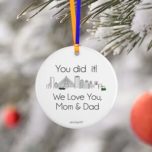 May include: White ceramic bauble with a black outline of a city skyline and the text "You did it! We love you, Mom & Dad".
