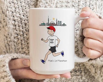 May include: White ceramic mug with a cartoon illustration of a runner in a red cap and black shorts, with a city skyline. The text "Mark's 1st Marathon" is below the runner. The mug has a white handle and the text "side 1" is on the side.