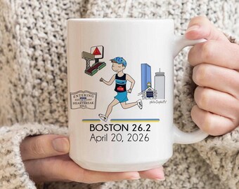 May include: White ceramic mug with a cartoon illustration of a marathon runner. The mug displays "BOSTON 26.2 April 20, 2026" and Boston landmarks. The runner is in blue shorts and a blue and black tank top. The mug has a white handle.
