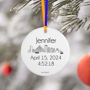 May include: White ceramic bauble featuring a black and white cityscape silhouette, the name "Jennifer", the date "April 15, 2024", and the time "4:52:18".