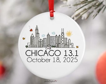 May include: White ceramic Christmas ornament with a red ribbon. The ornament features a black and white skyline of Chicago, Illinois, with the text "CHICAGO 13.1 October 18, 2025". The design includes hearts and a sun.
