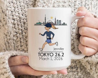 May include: White ceramic mug with a cartoon illustration of a runner in blue attire, a blue cap, and blonde hair. The mug displays the text "TOKYO 26.2 March 1, 2026" and the name "Jennifer", plus a Tokyo skyline design.