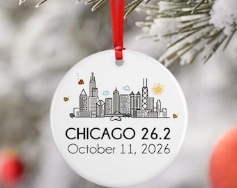 May include: White ceramic ornament with a red ribbon, featuring a black and white skyline of Chicago. The text "CHICAGO 26.2 October 11, 2026" is printed below the skyline. The ornament is decorated with small hearts and a sun.