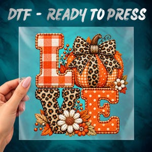 May include: A DTF ready to press transfer featuring the word LOVE. The L is orange and white gingham, the O is an orange pumpkin with a leopard print bow, the V is leopard print, and the E is orange with white polka dots and flowers.