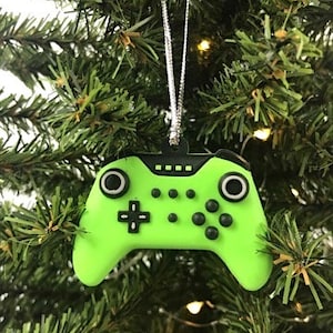 May include: A green and black video game controller ornament for a Christmas tree.