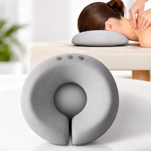 May include: A circular, light gray, textured massage device with a central opening and a vertical slit at the bottom. The top of the device features three circular control buttons with icons for power, heat, and intensity settings.
