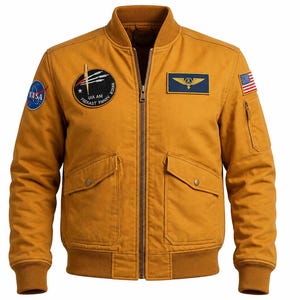 May include: A mustard yellow bomber jacket featuring a front zip, ribbed collar, cuffs, and hem. It includes a NASA patch, a circular mission patch, a rectangular wing emblem, and a small United States flag patch on the left sleeve.