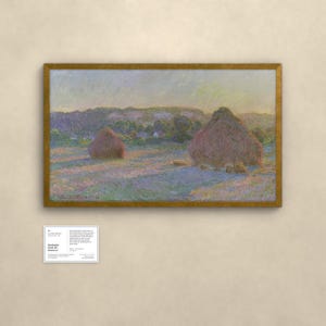 May include: A framed landscape painting depicting two large haystacks in a field at sunset, with soft purple and gold light casting long shadows across the grass. The artwork is signed Claude Monet 91 and includes a small informational placard.