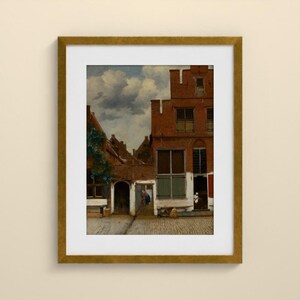 May include: A framed art print depicting a Dutch cityscape with red brick buildings, a cobblestone courtyard, and a cloudy sky. The scene features architectural details like multi-paned windows and arched doorways, presented in a gold-toned frame.