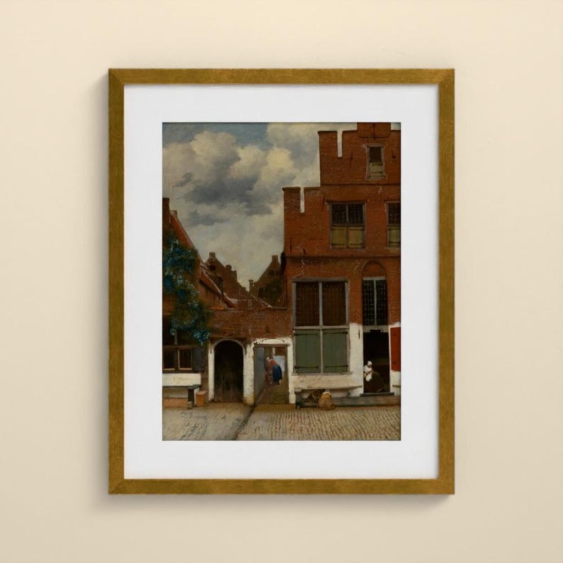 May include: A framed art print depicting a Dutch cityscape with red brick buildings, a cobblestone courtyard, and a cloudy sky. The scene features architectural details like multi-paned windows and arched doorways, presented in a gold-toned frame.