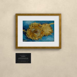 May include: A framed art print featuring two yellow sunflowers against a textured blue background, enclosed in a gold-toned frame with a white mat. Below the frame is a small black rectangular plaque with white text detailing the artwork.