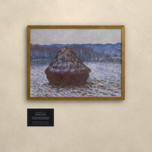 May include: A framed print of Claude Monet's Haystacks in Winter, featuring a dark brown haystack in a snowy field with blue-toned trees and mountains in the background. Below the artwork is a small black informational plaque with white text.