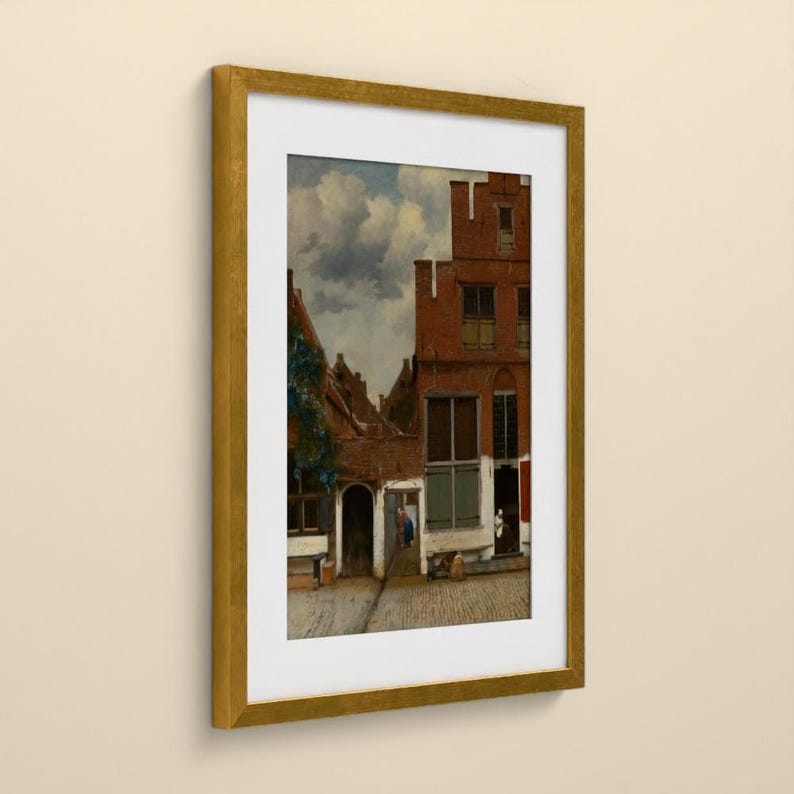 May include: A framed print of a painting depicting a narrow street with red brick buildings, arched doorways, and a cloudy sky. The artwork features a cobblestone path, green climbing vines on a wall, and small figures near the building entrances.