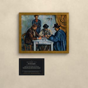 May include: A framed oil painting titled Die Kartenspieler by Paul C&eacute;zanne depicting four figures playing cards at a white table. Three figures are seated wearing hats and coats, while one stands behind them. A black informational plaque is positioned below.