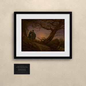May include: A framed art print featuring the painting Two Men Contemplating the Moon by Caspar David Friedrich. The image shows two figures standing on a rocky path under a gnarled tree, looking at a crescent moon in a dark, twilight sky.