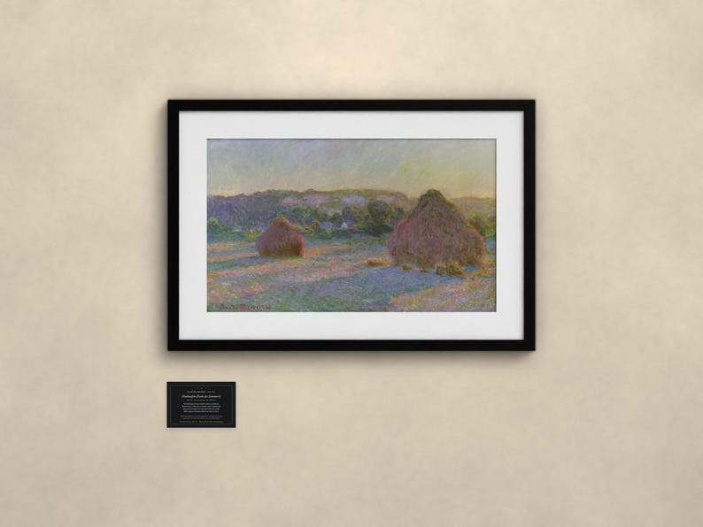 May include: A framed landscape painting depicting two large haystacks in a field under a soft, hazy sky. The artwork features muted tones of purple, yellow, and green. Below the frame, a small black plaque displays descriptive text.