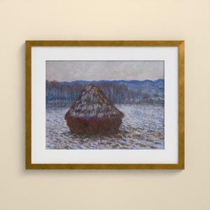 May include: A framed painting depicting a dark brown haystack centered in a snow-covered field. The background features a line of bare trees and distant blue hills under a pale sky. The artwork is enclosed in a metallic gold frame with a white mat.