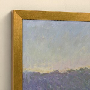 May include: A framed oil painting featuring a landscape with a field of purple flowers under a pale blue and yellow sky. The artwork is enclosed in a metallic gold frame with a textured finish, showcasing visible brushstrokes throughout the scene.